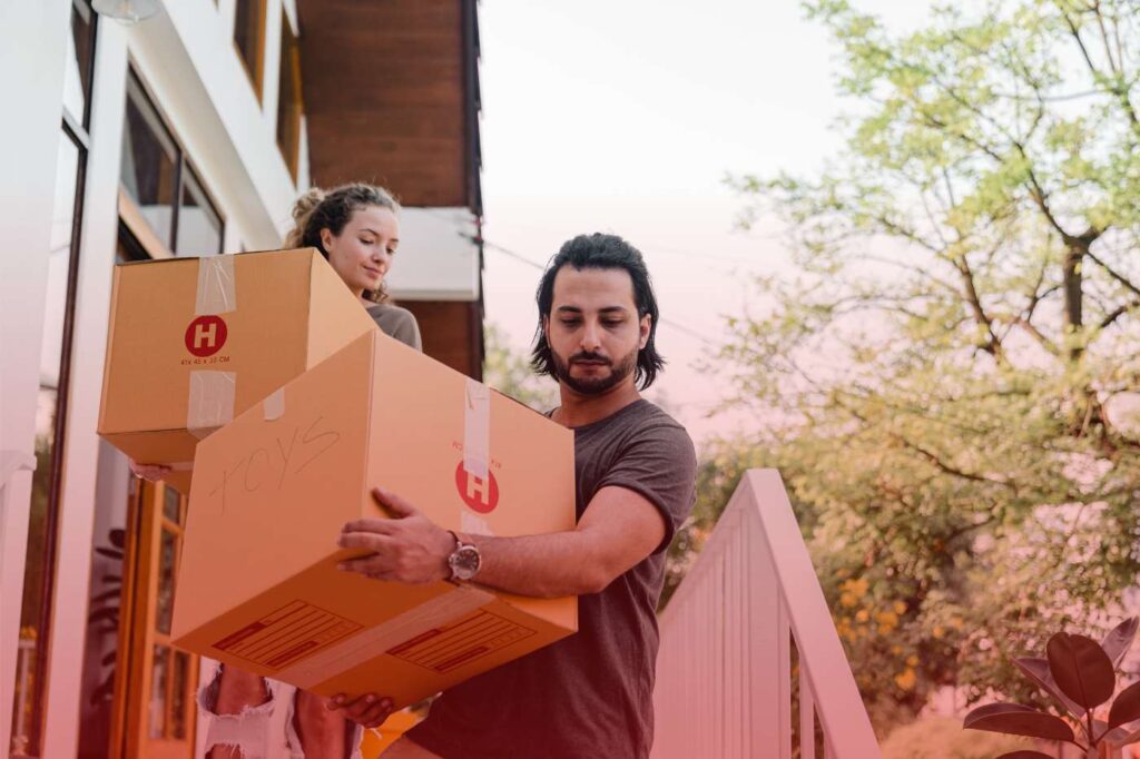 A man carrying moving boxes outside with a child sitting on top during a spring move.