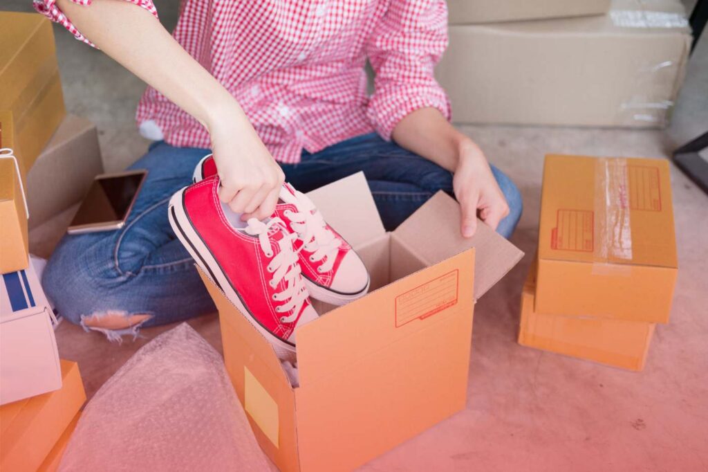 Individual placing red sneakers into a cardboard box while preparing for a move.