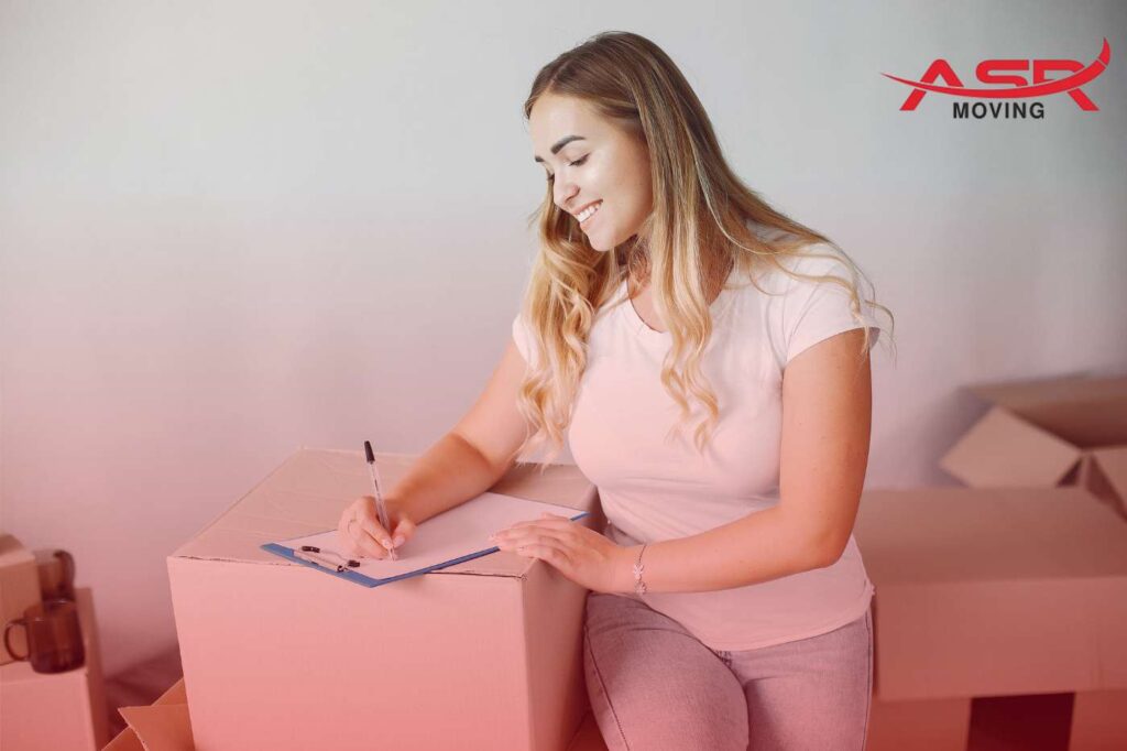 Woman writing on a clipboard checklist while surrounded by boxes