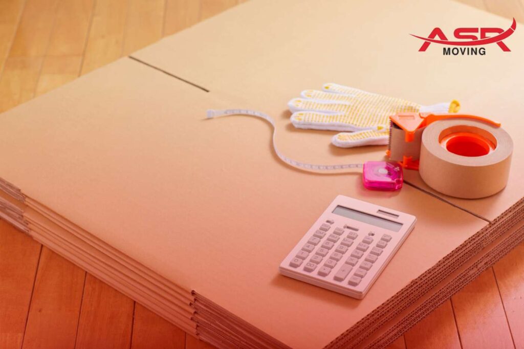 Packing supplies including tape, marker, cutter, and calculator placed on top of flat boxes.