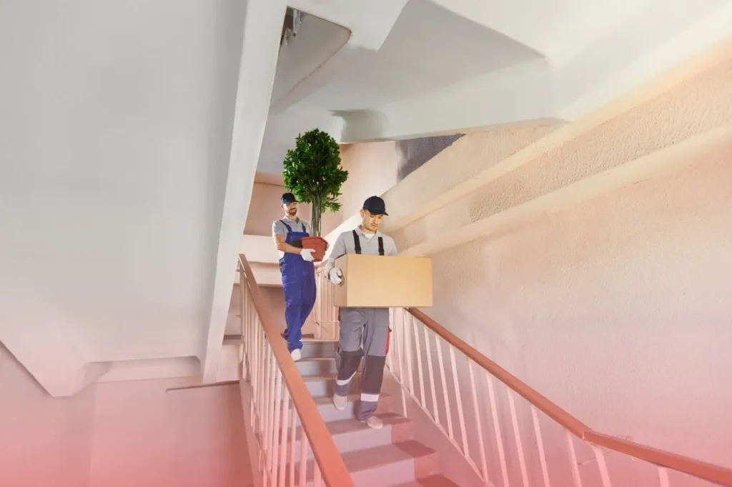 Two man each holding a box walking down the stairs